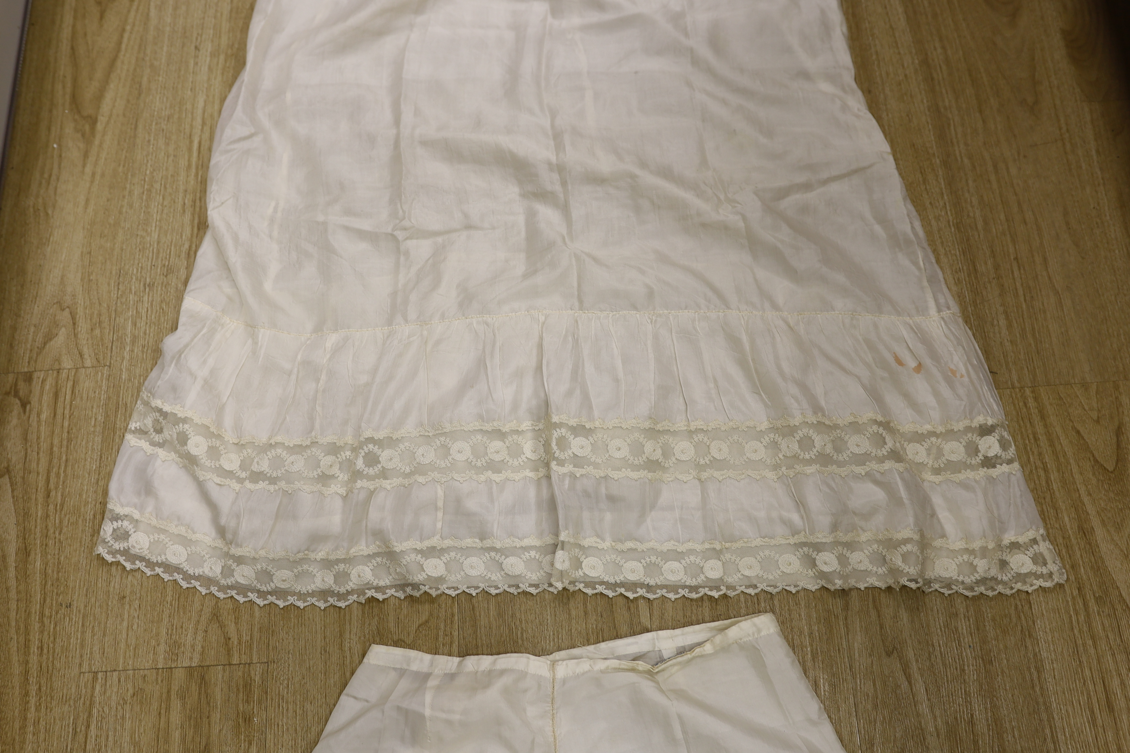 Two 1910-1920 cream silk and lace ladies floor length petticoats, one with a deep border of machine made Valenciennes lace, with a silk and satin ornamental rosette, the other a similar length, with bands of lace and sil